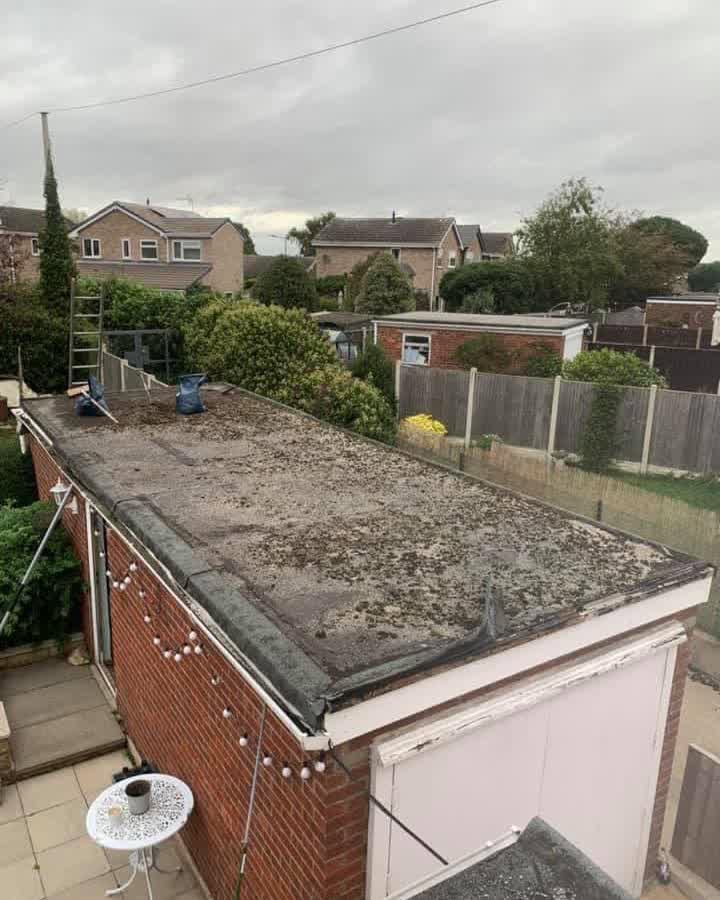 Old felt garage roof with standing debris, moss growth and a lifting edge trim before the work